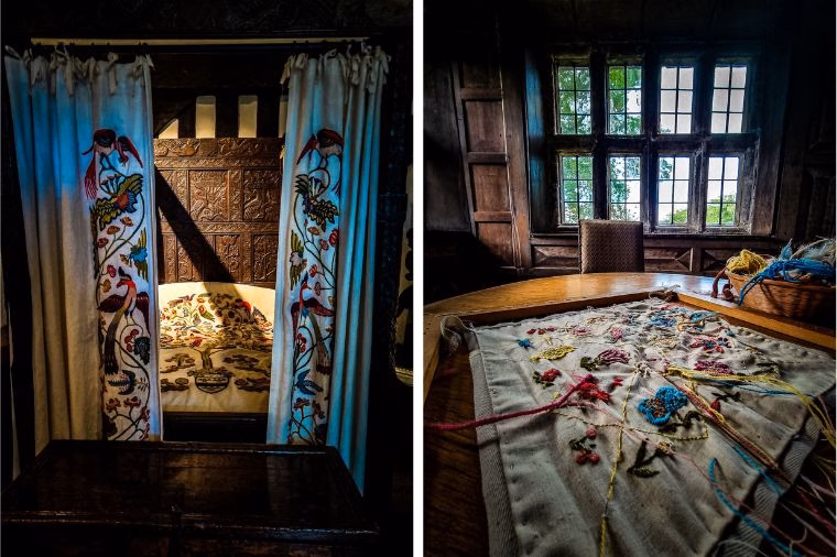 Split-panel photograph of embroidery at Oakwell Hall. The left side shows a dark wood four-poster bed framed by white curtains embroidered with colorful birds and floral patterns. The right side features a sunlit wooden room with a large window, a table covered in a partially completed embroidery piece with bright pink, blue, and yellow threads, alongside a basket of yarn.