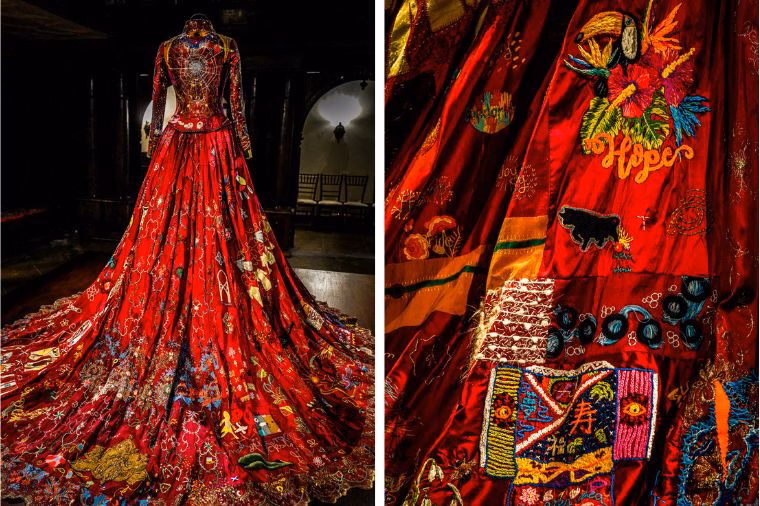 Full back view and embroidery close-up of The Red Dress from The Red Dress Project, on display at Oakwell Hall for the WOVEN in Kirklees Festival. The gown’s train cascades with embroidered messages and symbols like “Hope” and “Joy,” reflecting the global collaboration spotlighted in this Red Dress Exhibition Review and The Red Dress Project Review.