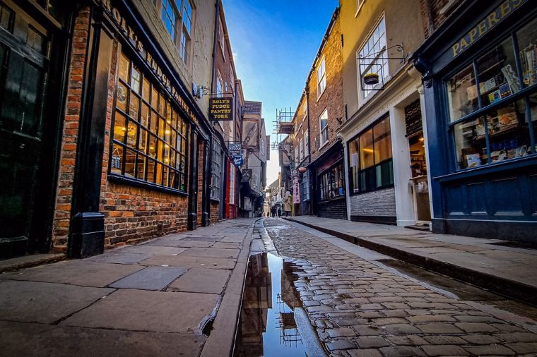 A quiet view along The Shambles in York, with its narrow cobbled street lined by historic timber-framed and brick buildings, independent shops and traditional shopfronts.